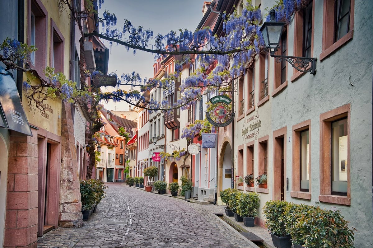 Eine Kopfsteinpflasterstraße, gesäumt von bunten Gebäuden und Blumen.
